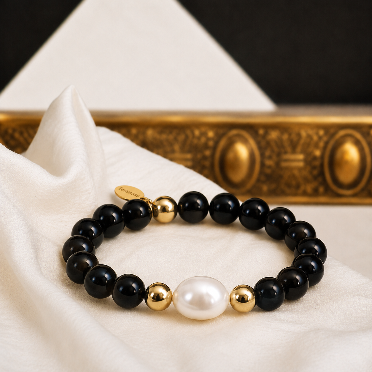 Teramasu Luxury Gratitude bracelet with black onyx beads, a baroque pearl, and gold-filled beads displayed on soft white fabric with elegant gold decor.