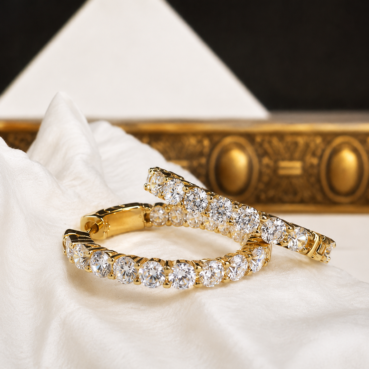 Teramasu Signature Travel Hoop Earrings in gold with clear crystals, displayed on white fabric in a luxury setting.